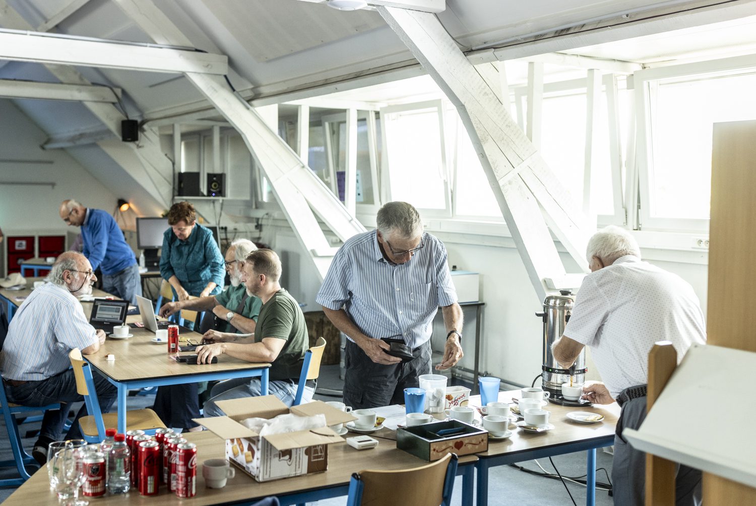 Koffiepauze in het clublokaal: leden schenken koffie in en praten bij rond de tafels.